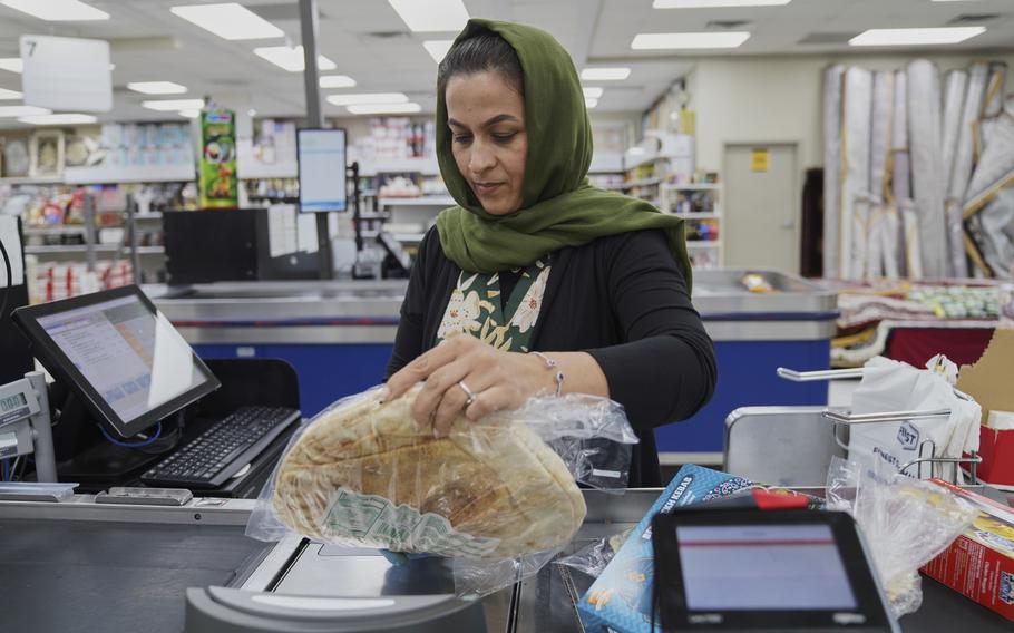 A woman wearing a head scarf holds an item over the scanner in a grocery store check-out line.