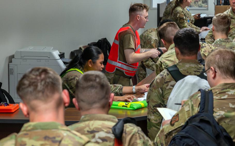 Airmen stand in line while other airmen behind a desk process them for deployment. 