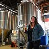 A woman holds a glass of beer in a brewery.