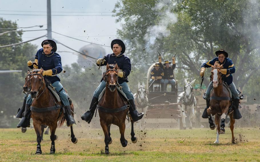 Soldiers in western-style blue cavalry uniforms ride horses at full gallop.