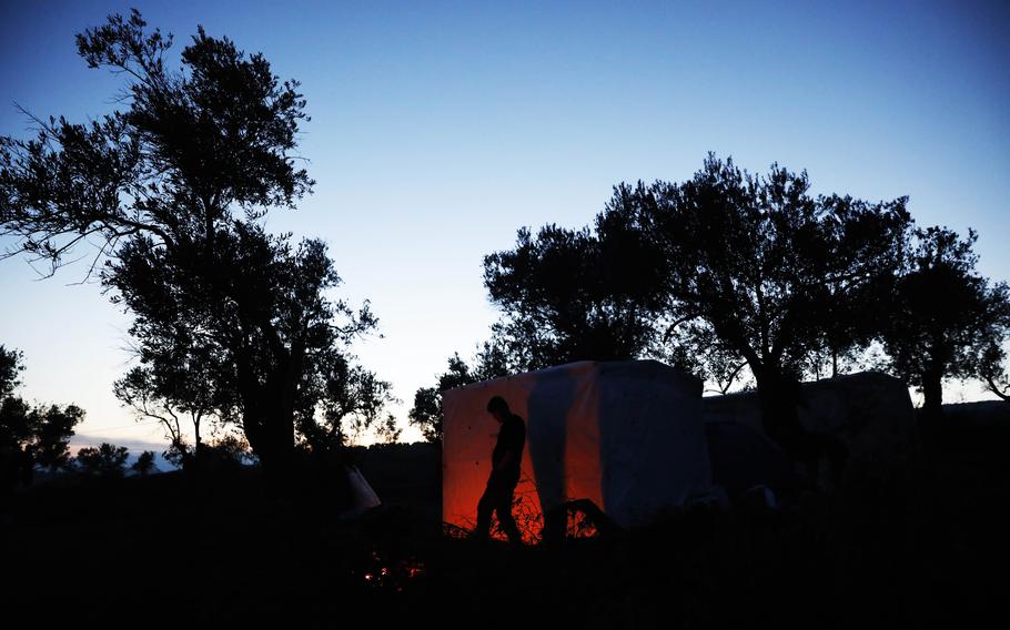 A migrant from Afghanistan warms himself on a fire at a migrant camp in Lesbos, Greece.