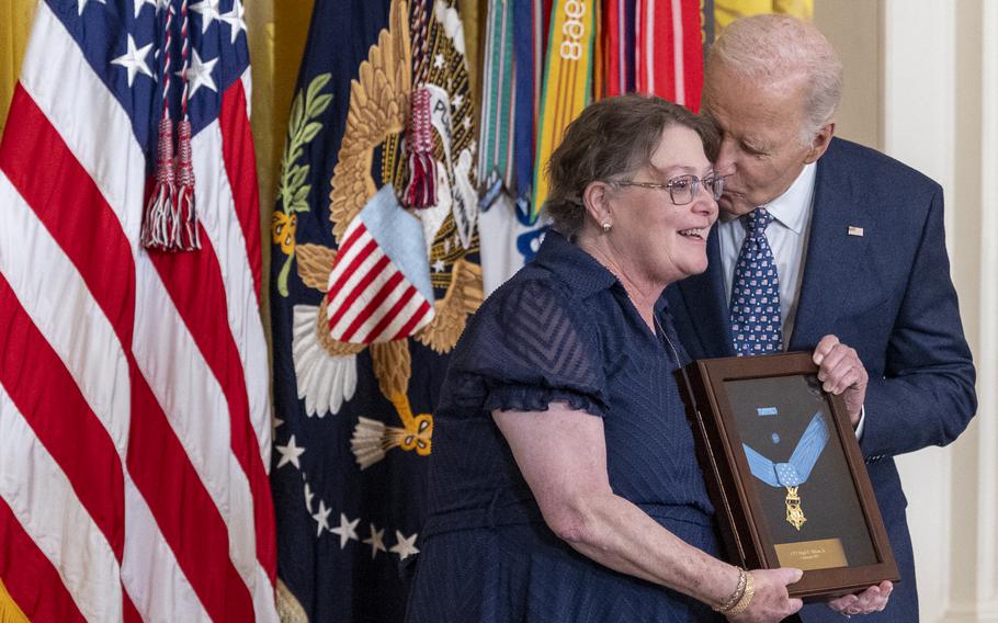 Joe Biden stands next to an elderly woman in glasses who holds a framed Medal of Honor award posthumously to her father.