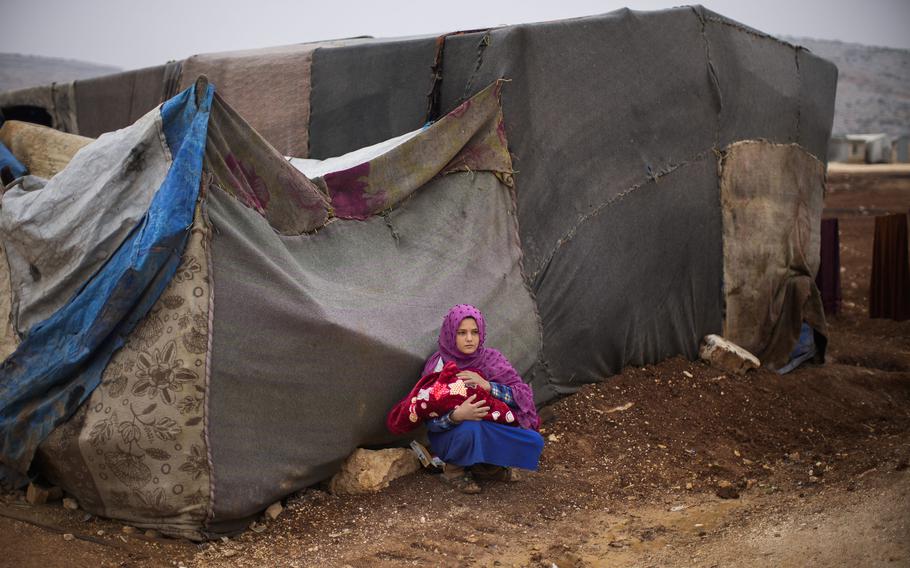 A Syrian young woman holds a baby in a refugee camp for displaced people supported by the Turkish Red Crescent in Sarmada district, north of Idlib city, Syria, Thursday, Nov. 25, 2021.