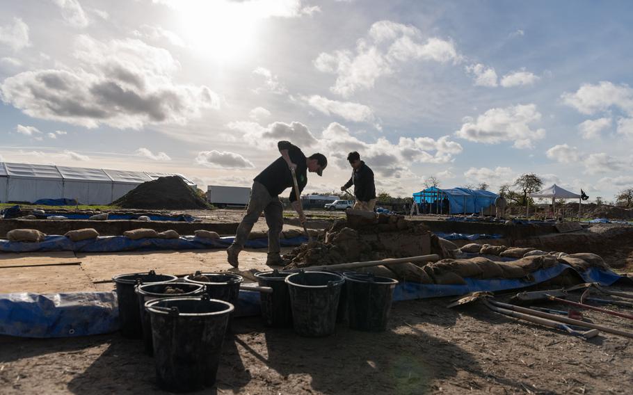 Army Cpl. Anthony Boulanger, left, and Army Spc. Alexis Jove, both with the 2nd Cavalry Regiment, shovel soil into buckets at an excavation site in Wistedt, Germany, Oct. 30, 2023. The soil will later be examined for airplane debris and potential human remains. 