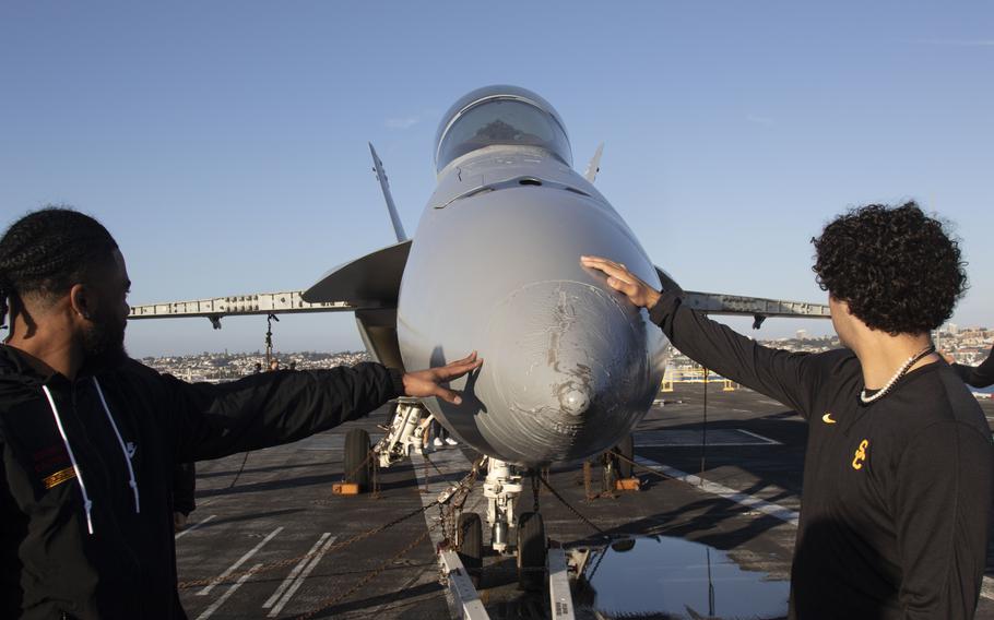 USC Trojans football team players touch an F/A-18E Super Hornet on Dec. 24, 2023, during an open ship tour aboard the Nimitz-class aircraft carrier USS Abraham Lincoln (CVN 72) prior to the 2023 Holiday Bowl. 
