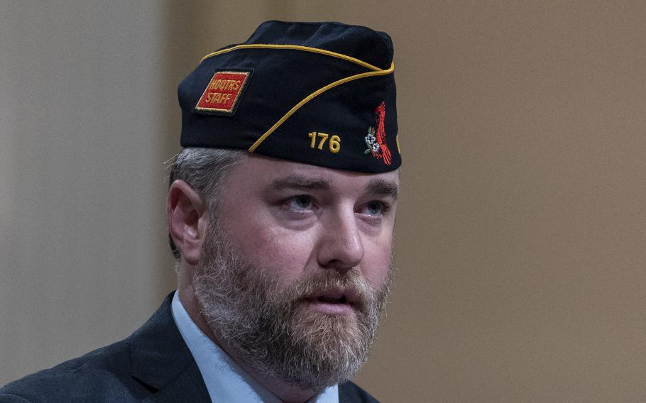 A man with a beard wearing a suit and a veterans cap.