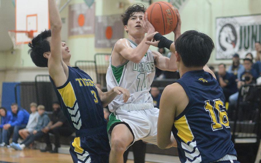 Kubasaki's Troy Harris skies for a shot between Taipei American defenders during Friday's inter-district boys basketball game. The Tigers won 61-41.