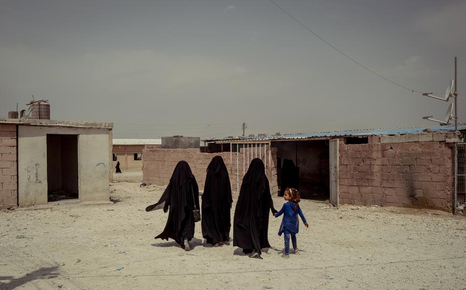 Three women and a child walk near the market in al-Hol camp. 