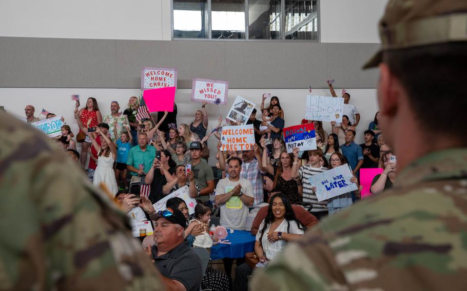 Soldiers face a crowd of friends and family holding signs.