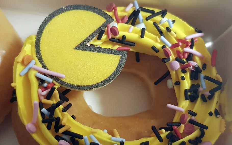 A close-up view of a doughnut with yellow icing, sprinkles and a yellow candy version of the Pac-Man video game character.