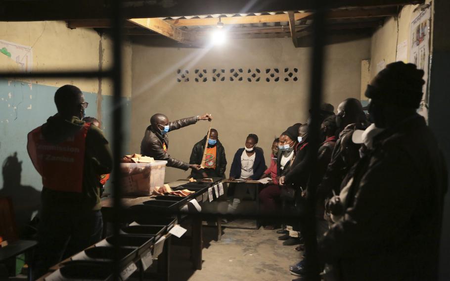 Political party agents keep a close eye as an electoral officer displays a ballot paper at the start of the counting process at a polling station in Lusaka, Zambia, Thursday Aug, 12, 2021. 