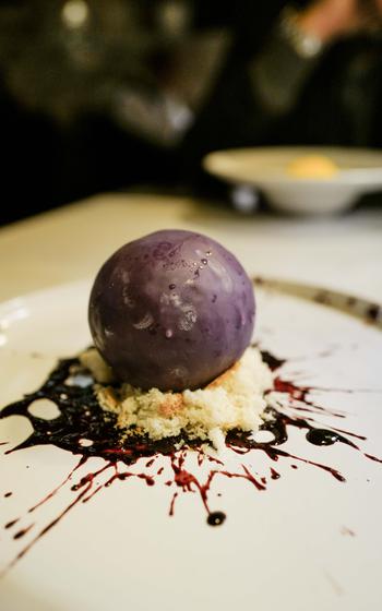 The blueberry bomb dessert features blueberry ganache and a core of wild blueberry jelly, creatively presented at Grifo Restaurant in Kerzenheim, Germany, to look like a splattered blueberry on a white plate.