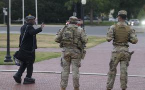 Armed National Guard members talk with a man.