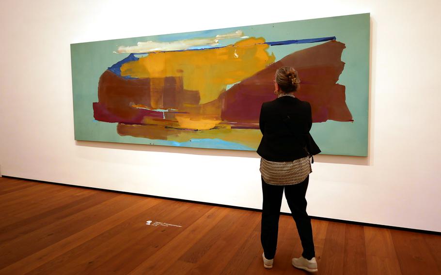 A woman looks at a painting on a museum wall.