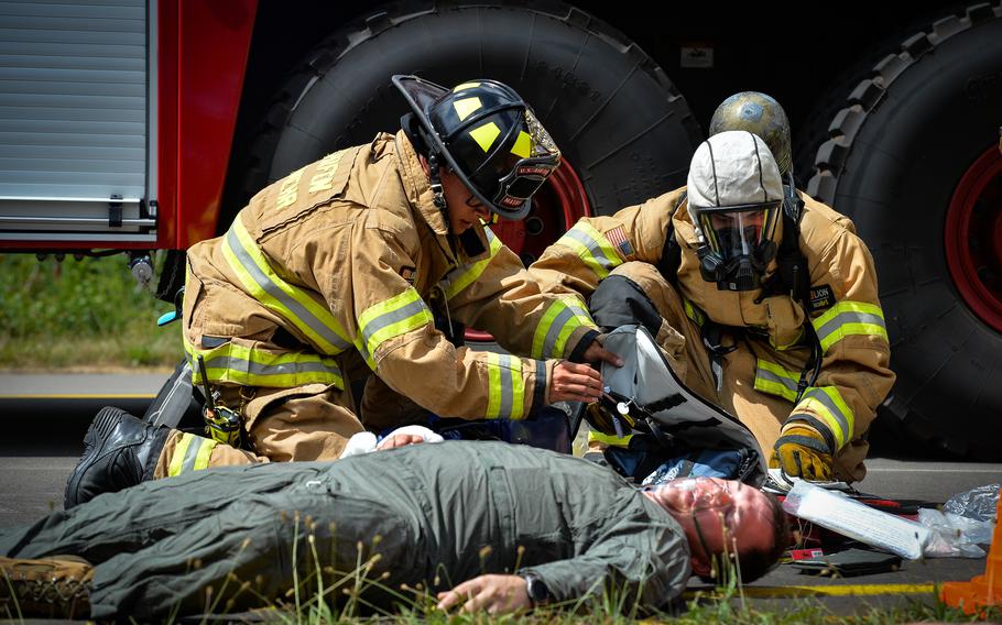 Senior Airman Philip Mathys, left, and a fellow firefighter with the 86th Civil Engineer Squadron provide first aid to Tech. Sgt. James Bennett, who played the victim at the scene of a simulated aircraft crash during Operation Varsity, a recurring emergency exercise at Ramstein Air Base, Germany, July 26, 2022.