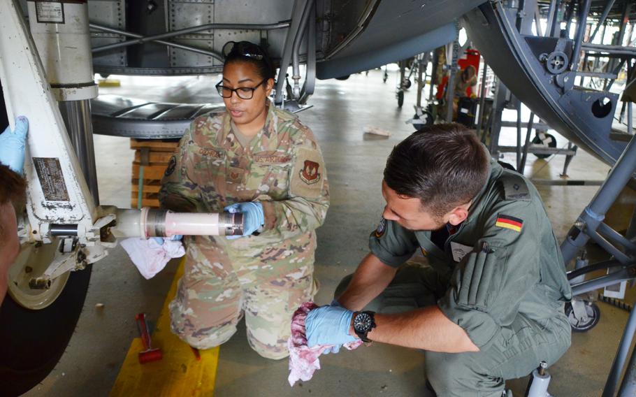 Air Force Tech Sgt. Hazel Cochran, left, cleans the axle of a C-130J's nose landing gear wheel as showing German military academy cadet Tom Palzer how to remove a tire from the plane at Ramstein Air Base on July 15, 2021.