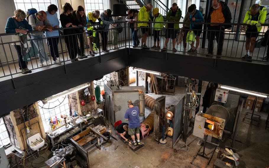 Visitors at a glass workshop watch as staffers make a glass object.