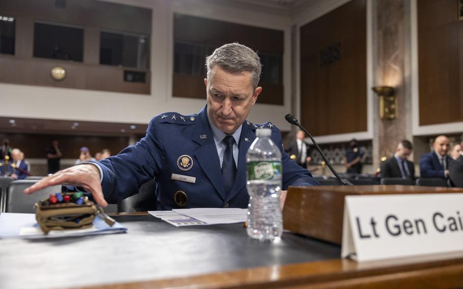 Caine in uniform seated and reaching for a small case.