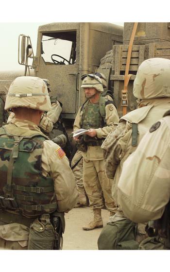 A vertical photo of soldiers by an armored truck.