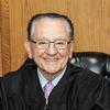 A judge smiles while sitting in a chair.