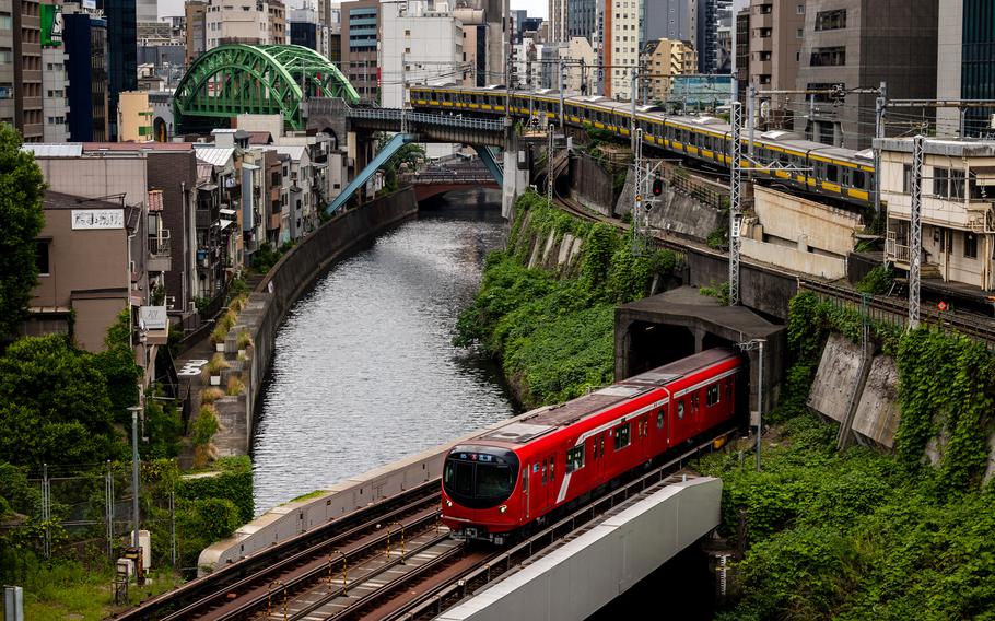A train exits a tunnel, crossing a bridge over a river.