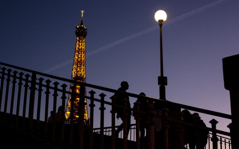 People walk on a bridge next to the Eiffel Tower in Paris, Wednesday Feb. 9, 2022.