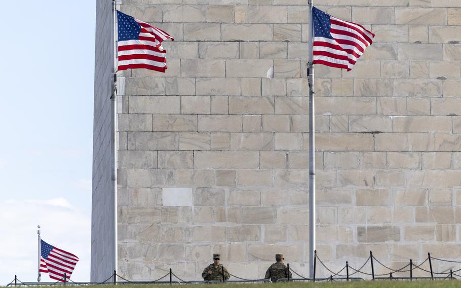 The small shapes of two soldiers from the chest up seen from a distance, near the base of the Washington Monument.