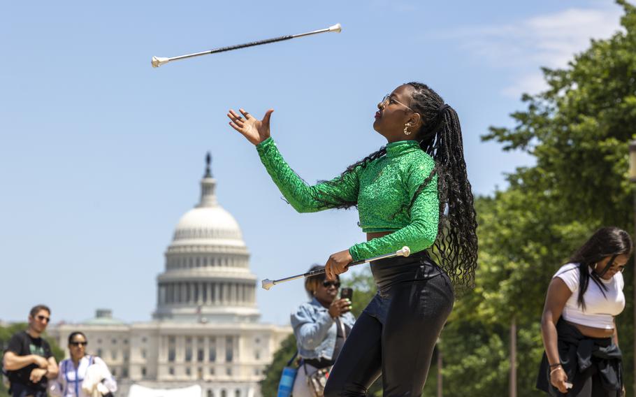 A young woman waits for the baton, in midair, to come down so she can catch it.