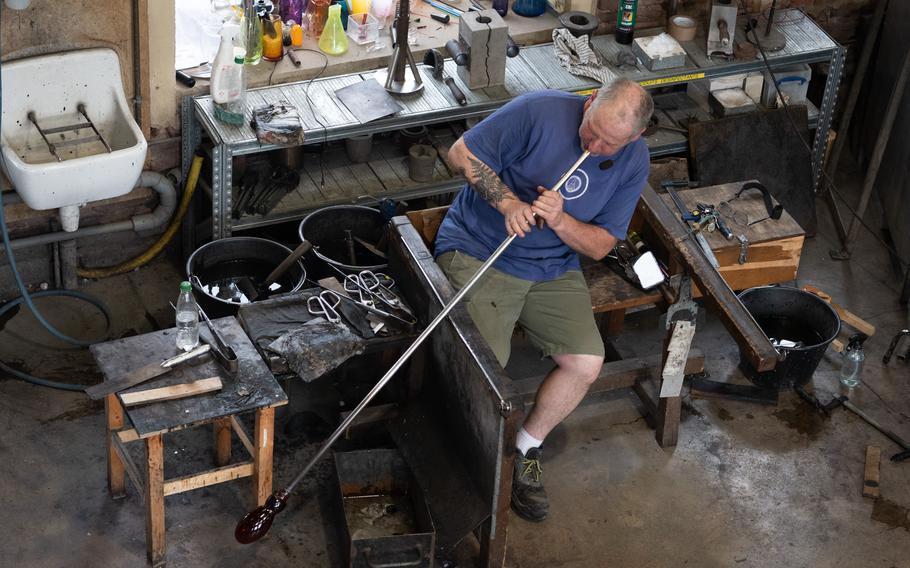 A craftsman uses a blowpipe to create a glass object.