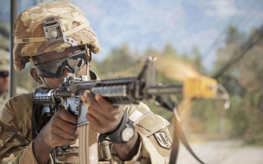 A soldier aims a rifle, with the camera closer to the rifle muzzle.