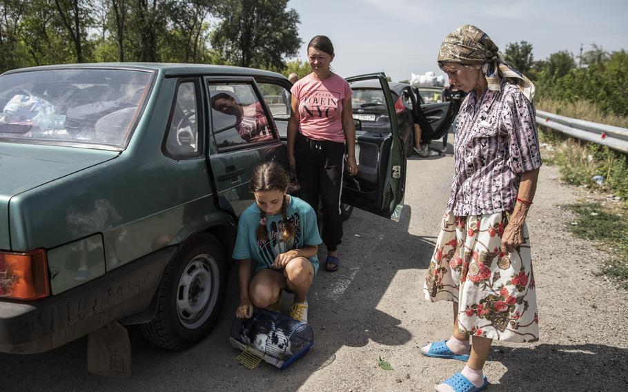 A family waits with their pet rabbit by their car among a convoy of other cars that have traveled from Russian controlled territory to a staging area controlled by Ukraine on the outskirts of the village of Kamiyanske on Aug. 27, 2022.