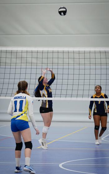Ansbach’s Georgia Bryant sets the ball for teammate Klea Russell during the 2022 DODEA-Europe Volleyball Tournament Oct. 29, 2022, at Ramstein Air Base, Germany. Sigonella’s Isabella Naselli stands ready across the net.