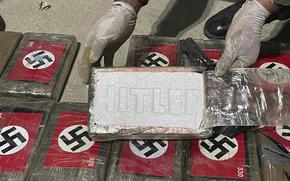 In this photo provided by the Peruvian Anti-Drug Police, an officer shows blocks of cocaine marked with Nazi swastikas and stamped with the name "HITLER", at the port of Paita, Piura region, Peru, Thursday, May 25, 2023. The police found more than 50 blocks of cocaine that were stashed in a container destined for a ship that was sailing for Belgium. 