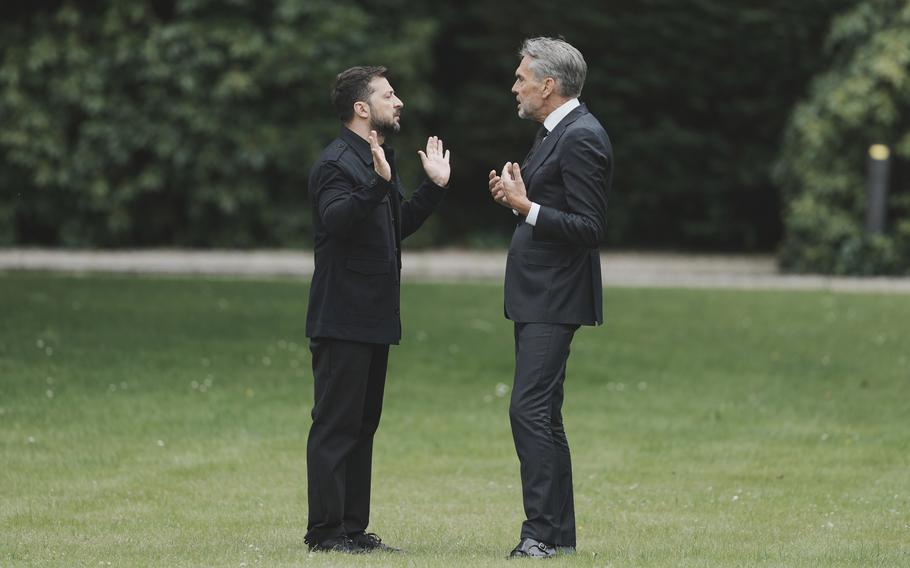 Two men in suits speak, each of them gesturing with both of their hands.