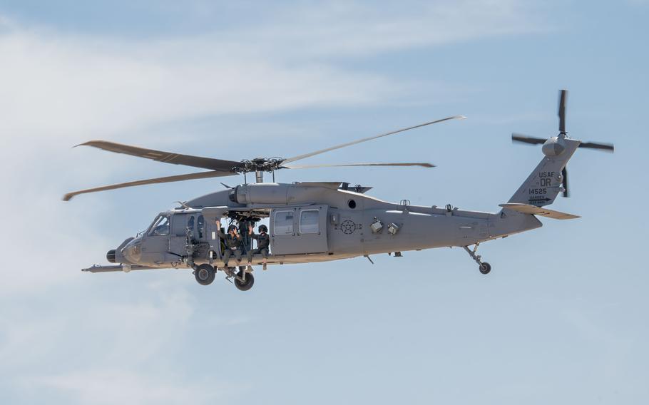 Two people sitting on the edge of a helicopter in the sky 