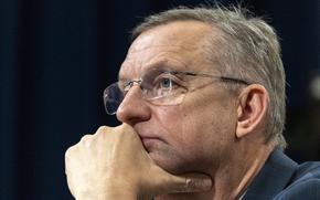 Close-up view of a man wearing glasses and resting his chin in his hand.