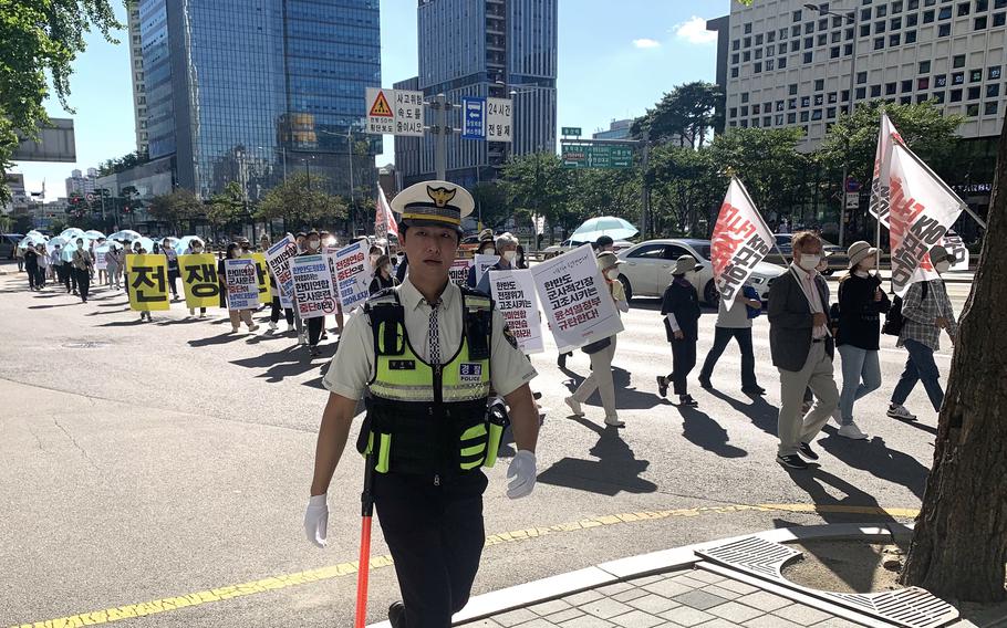 A South Korean police officer walks alongside anti-war protesters marching in Seoul, South Korea, Aug. 27, 2022.