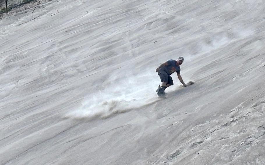 A man rides a snowboard down a hill made of sand.