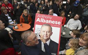 Australia's Prime Minister-elect Anthony Albanese, center, signs a poster for twin brothers Dimitri and Stavros, bottom right, as he visits a coffee shop in suburban Marrickville, Sydney, Sunday, May 22, 2022. Albanese has promised to rehabilitate Australia's international reputation as a climate change laggard with steeper cuts to greenhouse gas emissions. (Dean Lewins/AAP Image via AP)