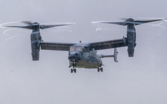 A V-22 Osprey tiltrotor aircraft flies through overcast skies with its twin rotors in horizontal position for forward flight. 