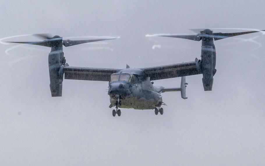 A V-22 Osprey tiltrotor aircraft flies through overcast skies with its twin rotors in horizontal position for forward flight. 