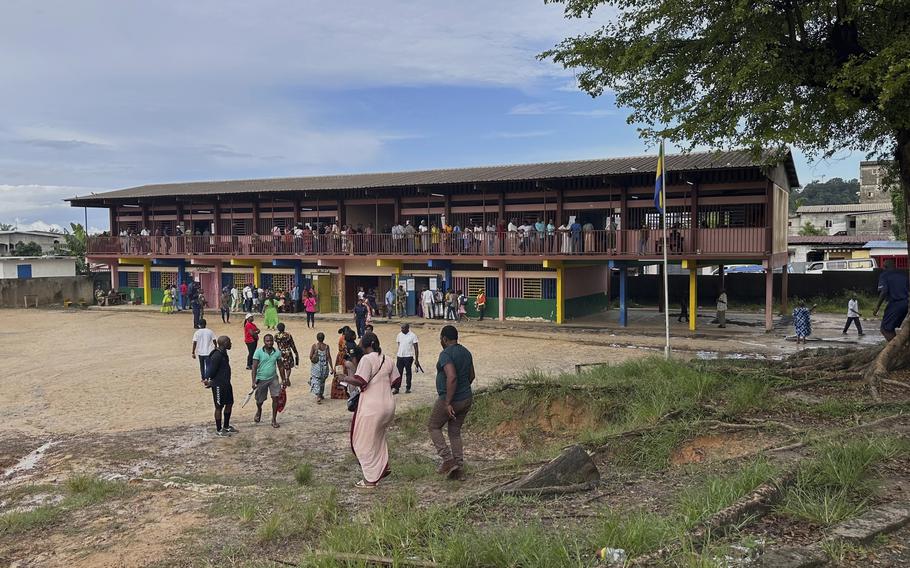 A wide building seen from a distance, full of people lining up.