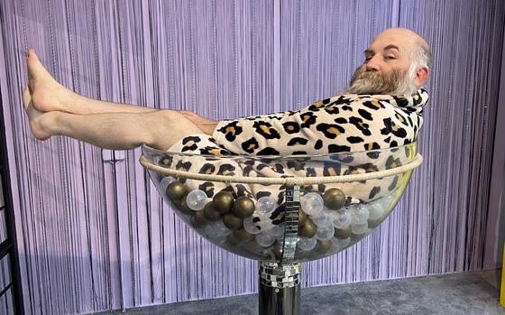 Chad Garland luxuriates in a giant Champagne glass Thursday, Oct. 21, 2021, inside SnapMySelf, a ''selfie museum'' in downtown Kaiserslautern where visitors can choose from nearly two-dozen sets or backdrops for their social media-ready self-portraits.