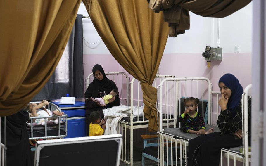 Women sit next to or hold young children on hopistal cots.