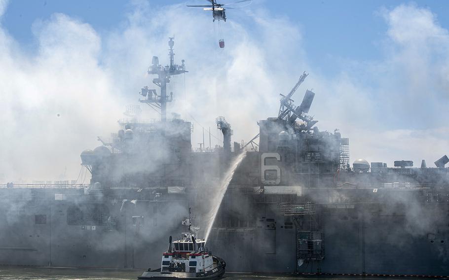 An MH-60S Seahawk helicopter provides aerial firefighting support alongside sailors and civilian fire crews on the ground in San Diego on July 13, 2020, as they fight the fire aboard amphibious assault ship USS Bonhomme Richard (LHD 6).