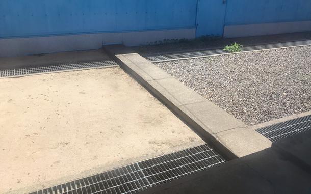 A narrow slab of concrete, seen from above, marking the border between South and North Korea sits across a walkway with gravel on one side, dirt on the other and a blue wall behind it.