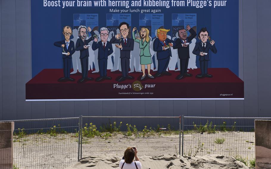 A woman taking a photo of a drawing of various NATO leaders.