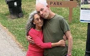 An elderly couple poses with their arms around each other.