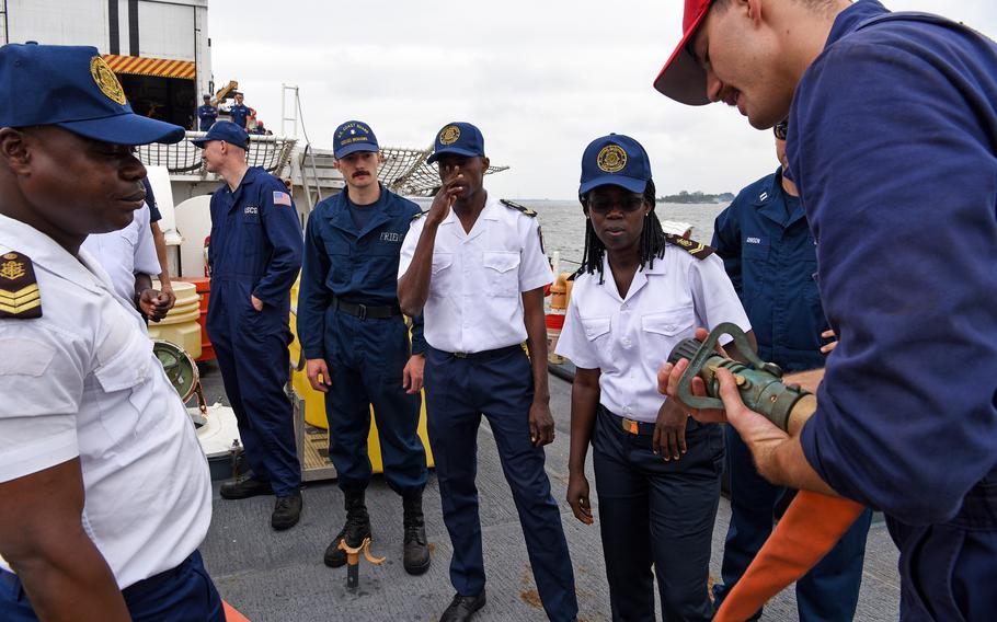 U.S. Coast Guard Ensign Thomas Wahlin, right, demonstrates how to operate a firefighting hose nozzle for Ivory Coast navy personnel during a damage control exchange aboard USCGC Mohawk in Abidjan, Aug. 13, 2022. 