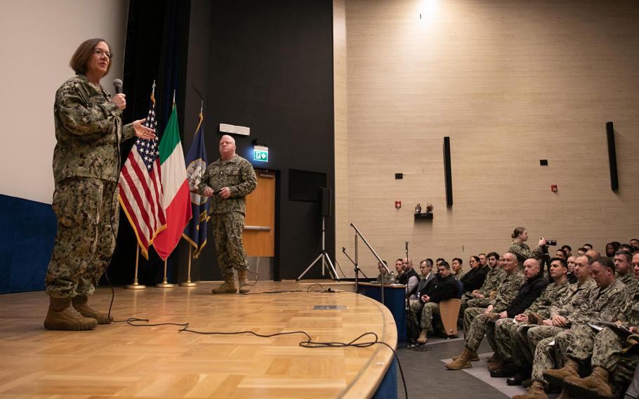 Chief of Naval Operations Adm. Lisa Franchetti speaks to sailors and civilians during a visit to Naples, Italy, Jan. 22, 2024, Listening on stage is Master Chief Petty Officer of the Navy James Honea.